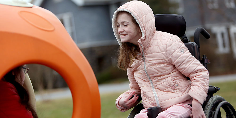 Female student in wheelchair smiles at another student on playground